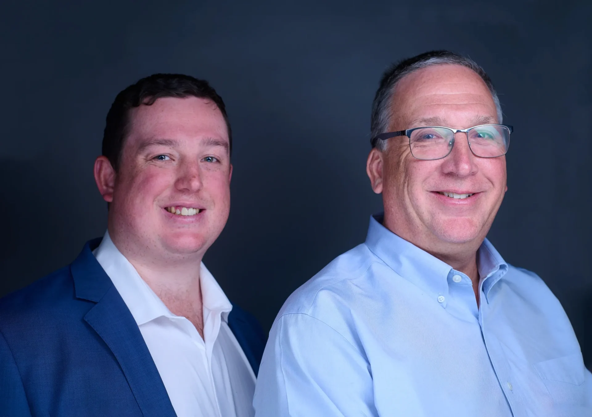 Two men standing next to each other in front of a black background.